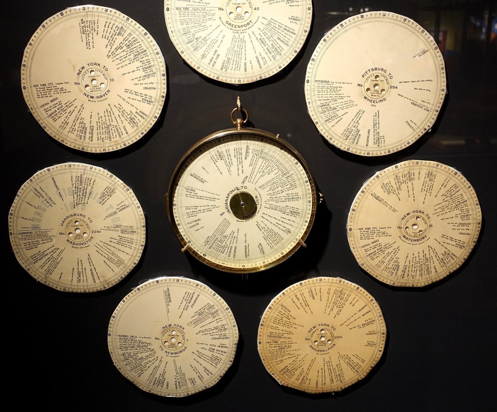 A display of discs with names of points on journeys around the circumference. The central disc - with seven other arranged around it - is in a round brass case. The journeys are mostly from New York to other towns and cities such as Philadelphia and New Haven. Other jouneys are Harrisburg to Washington and Pittsburgh to Wheeling.